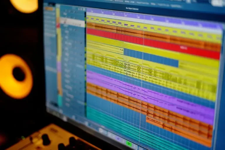 Ecran d'ordinateur affichant une session de montage audio dans Cubase, avec plusieurs pistes audio et midi colorées visibles, en arrière plan, des haut parleurs de monitoring de couleur orange, maoenligne