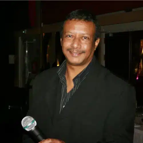 Photo de moi, souriant tenant un microphone, vêtu d'une veste noire, pris dans un environnement intérieur avec une ambiance chaleureuse